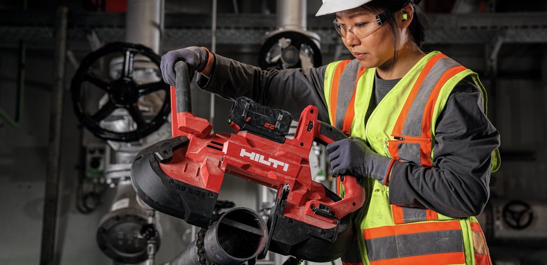 Mulher usando uma serra de fita para cortar um cano de metal